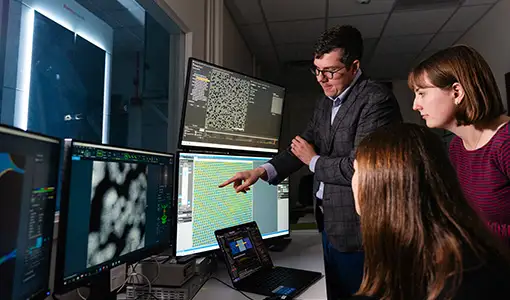 Continue reading about A man and woman standing and a woman seated, all looking at scientific information on multiple computer monitors.
