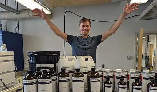 Evan raises his arms, palms down, over a collection of containers with the name, “Zila Bioworks” written on them.