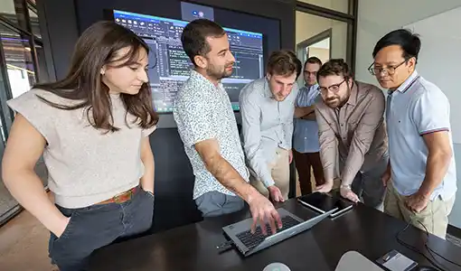 Continue reading about Six people stand around a computer.