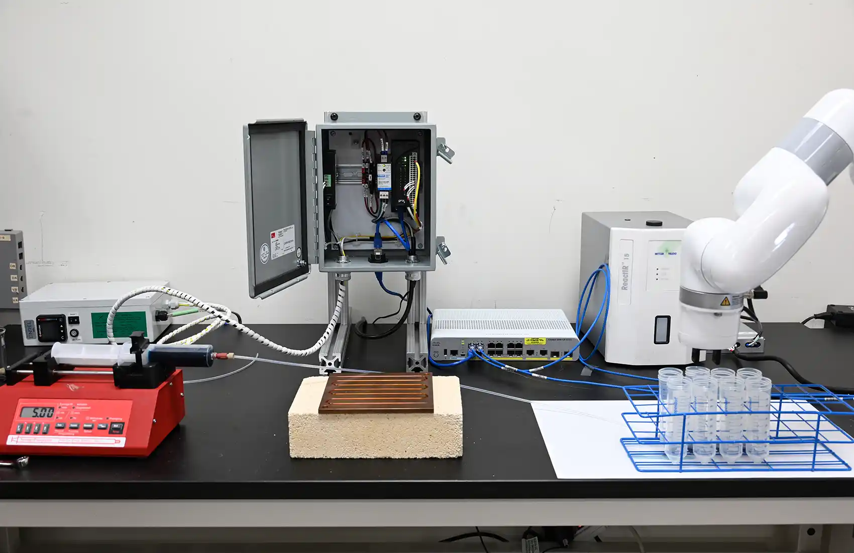 An experimental setup using automated flow chemistry processes, including a robotic arm and an array of syringe pumps.