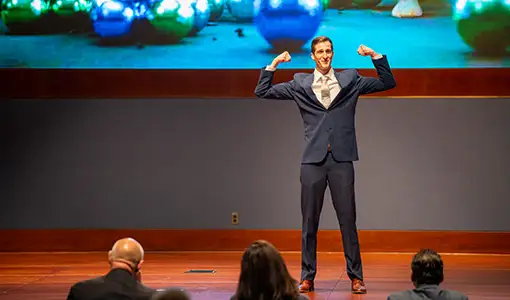 Continue reading about A person in a suit flexes his arms on stage