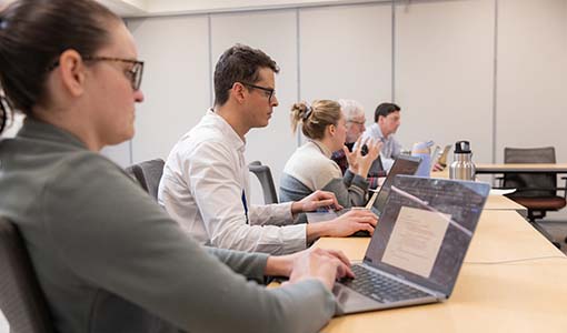 Continue reading about Five people seated at a conference room table while using laptop computers