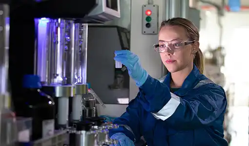 Continue reading about A person wearing gloves and safety goggles holds up a container in a lab.