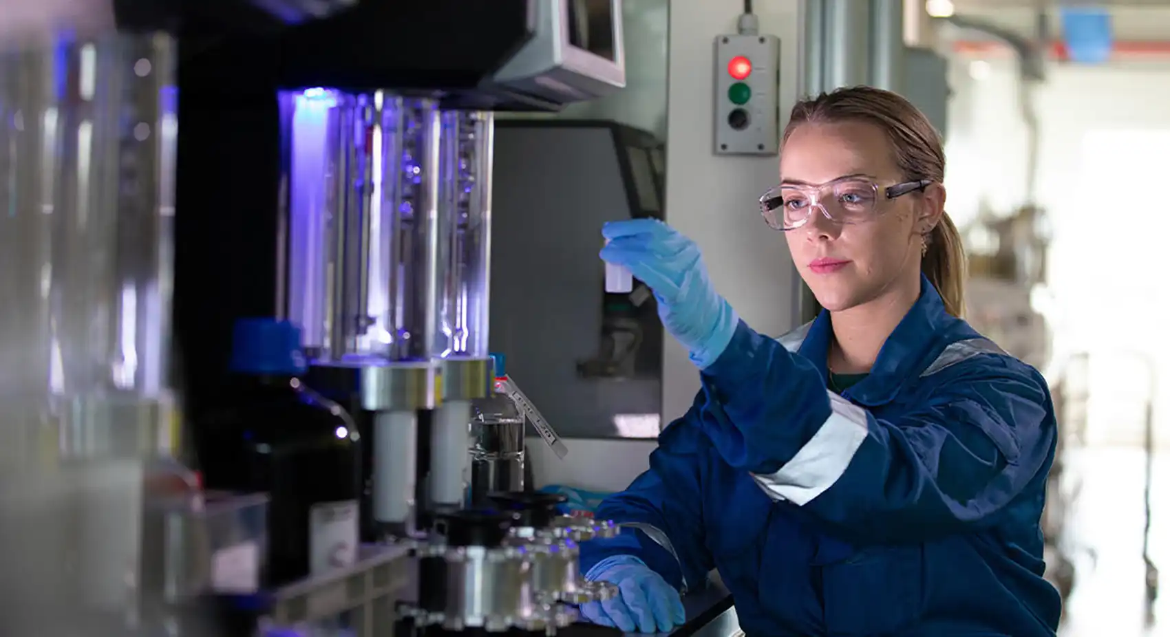 20260716-nlr-and-exxonmobil-launch-accelerate-program-for-advanced-materials-innovators A person wearing gloves and safety goggles holds up a container in a lab.