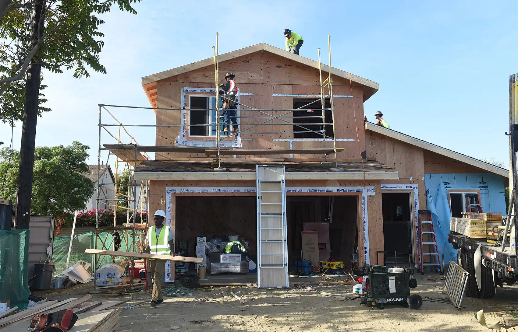 20260720-affordable-homes-cooling-centers-faster-grid-yes-please-habitat-la A home under construction with three men in hardhats working on different areas of the home.