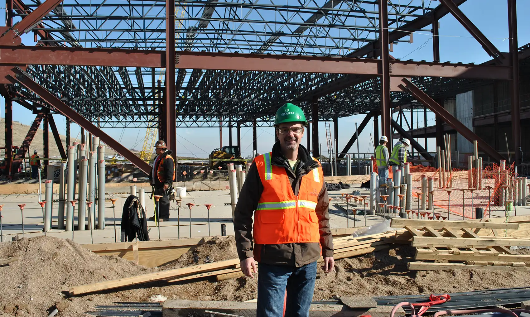 A person in a construction vest and hard hat standing in front of a construction site.