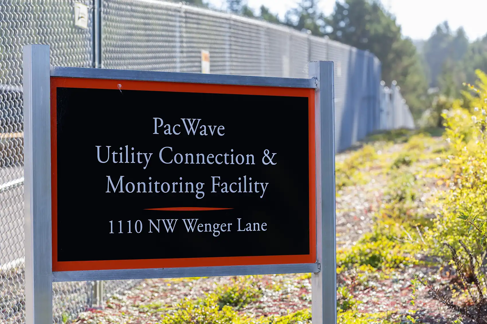 20260909-pacwave-opens-a-giant-leap-for-marine-energy-9U3A5307 A sign in front of a chain-link fence reads, “PacWave Utility Connection & Monitoring Facility, 110 NW Wenger Lane.”