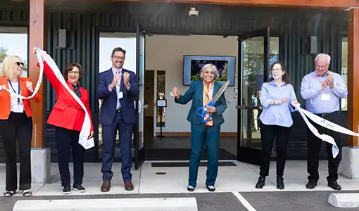 Continue reading about A photo of six people celebrating at the front entrance of a building. In the center, a person holds oversize scissors.