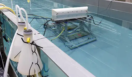 Continue reading about A wave tank in a laboratory showing the underwater testing apparatus inside the tank.