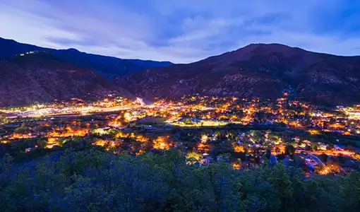 Continue reading about Overlooking town lit up at twilight with mountains in background.