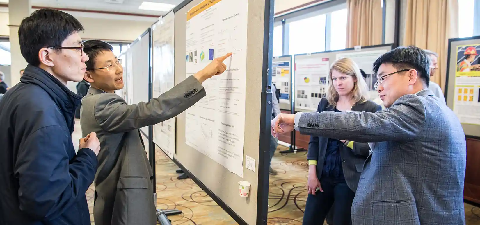 Researchers point to posters on a wall and share presentations with workshop participants.