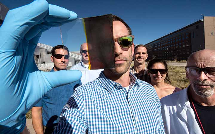 Six authors pose together. The person in front holds a sample of a switchable photovoltaic window.