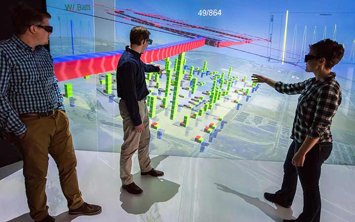 Three engineers use a 3D energy model to discuss potential energy loads of the proposed development growth.