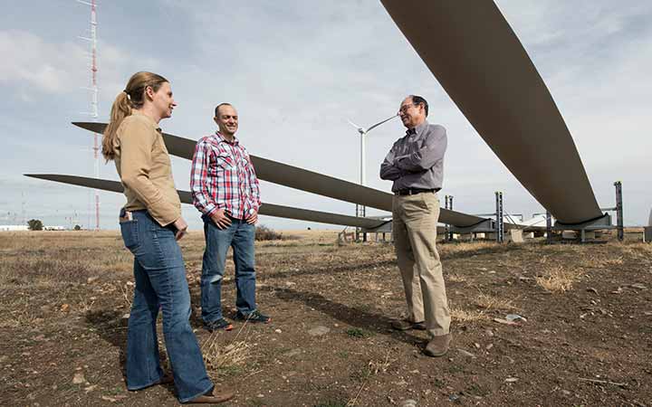 Three software co-authors stand underneath large wind turbine blades in a field outside.