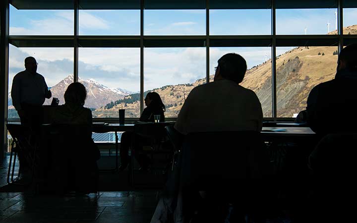 Silhoutted workshop participants with large windows showing mountains in the background.