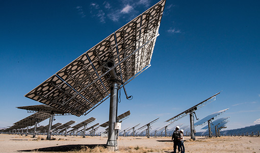 Two workers looking underneath a large concentrating solar power array in a desert area.