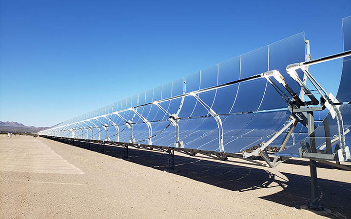 Curved, mirrored panels reflecting sunlight in a desert with mountains in the background