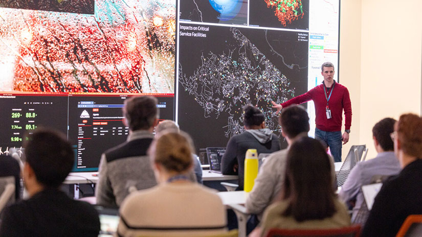 Person presenting charts and data on screen in front of full room