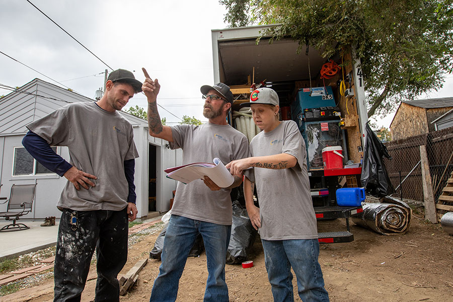 three people stand together talking and pointing at something in the distance.