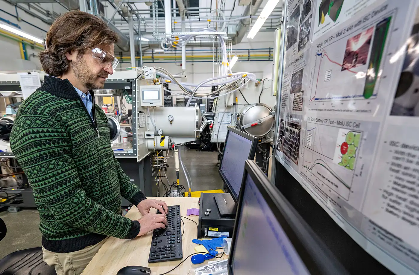 A person wearing safety goggles works on a computer in a lab.