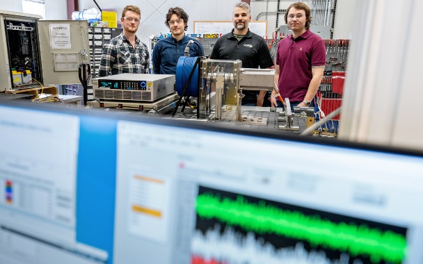 Group of people stand in a lab behind computer screens displaying data