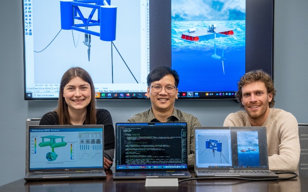 Three people stand behind laptops with data on the screens