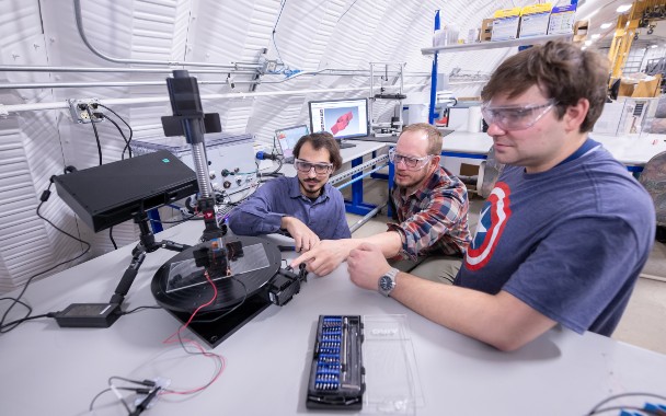 Three people work on marine technology device in lab