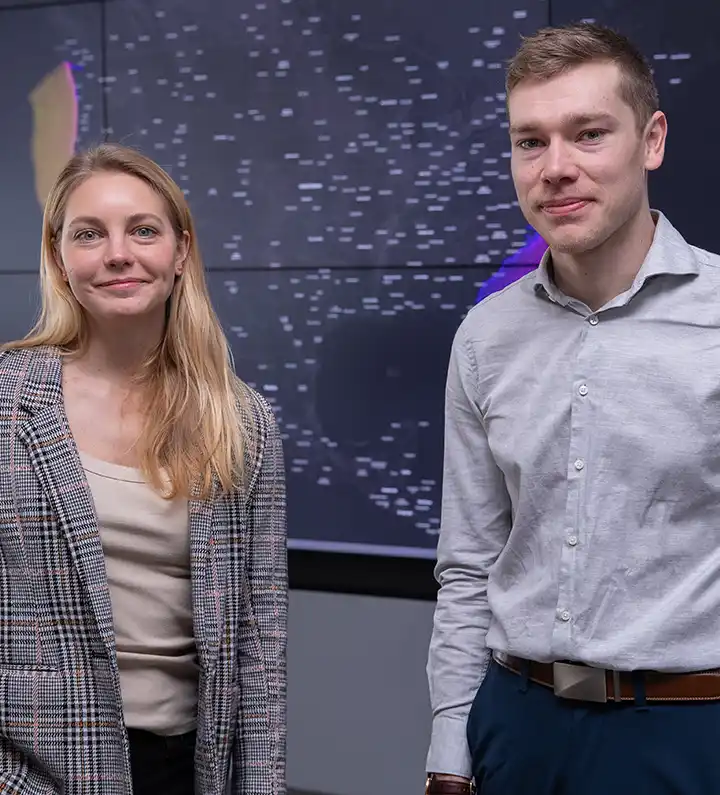 Two researchers stand in front of large data display screen