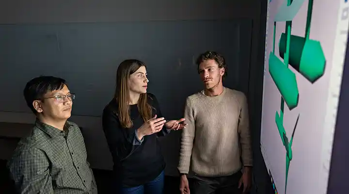 Three people look at model data on large display screen.