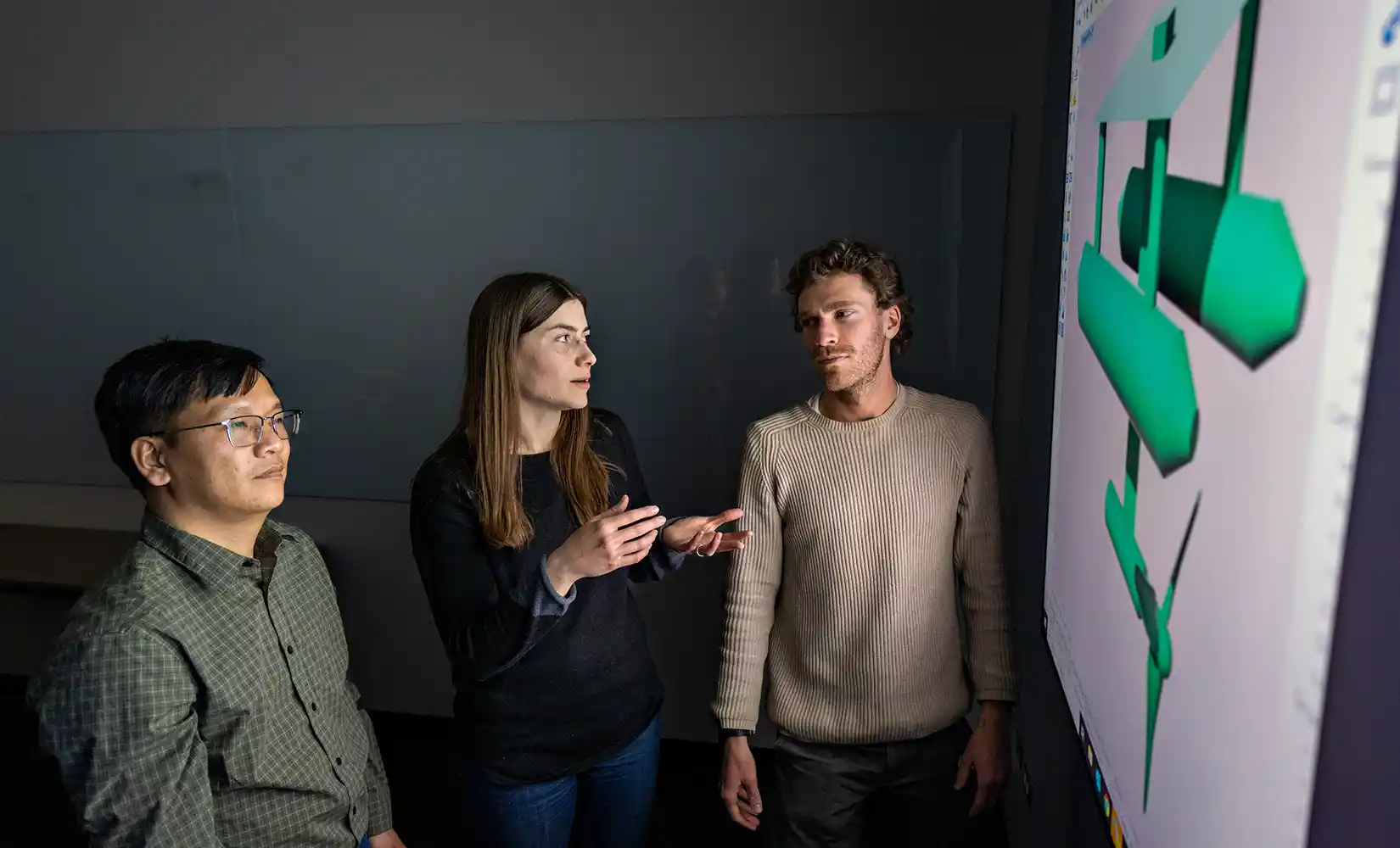 Three people look at model data on large display screen.