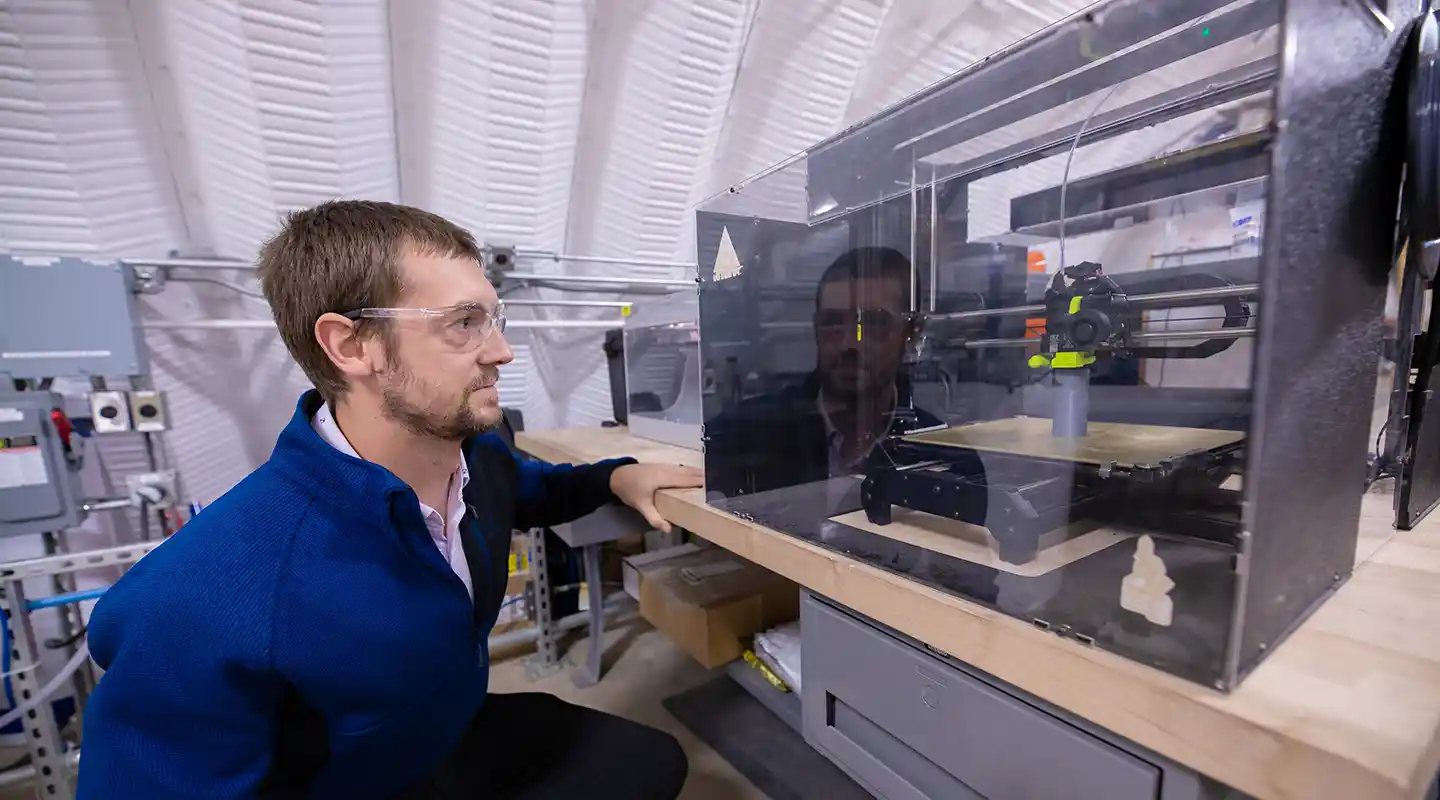 Researcher examines a 3D printer in process.