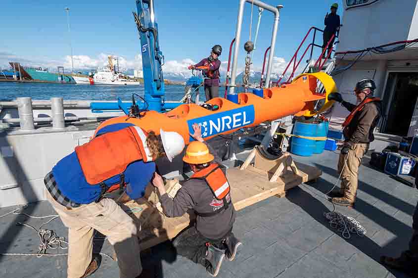 Four people in hard hats on a dock adjust a buoy bearing the NLR logo