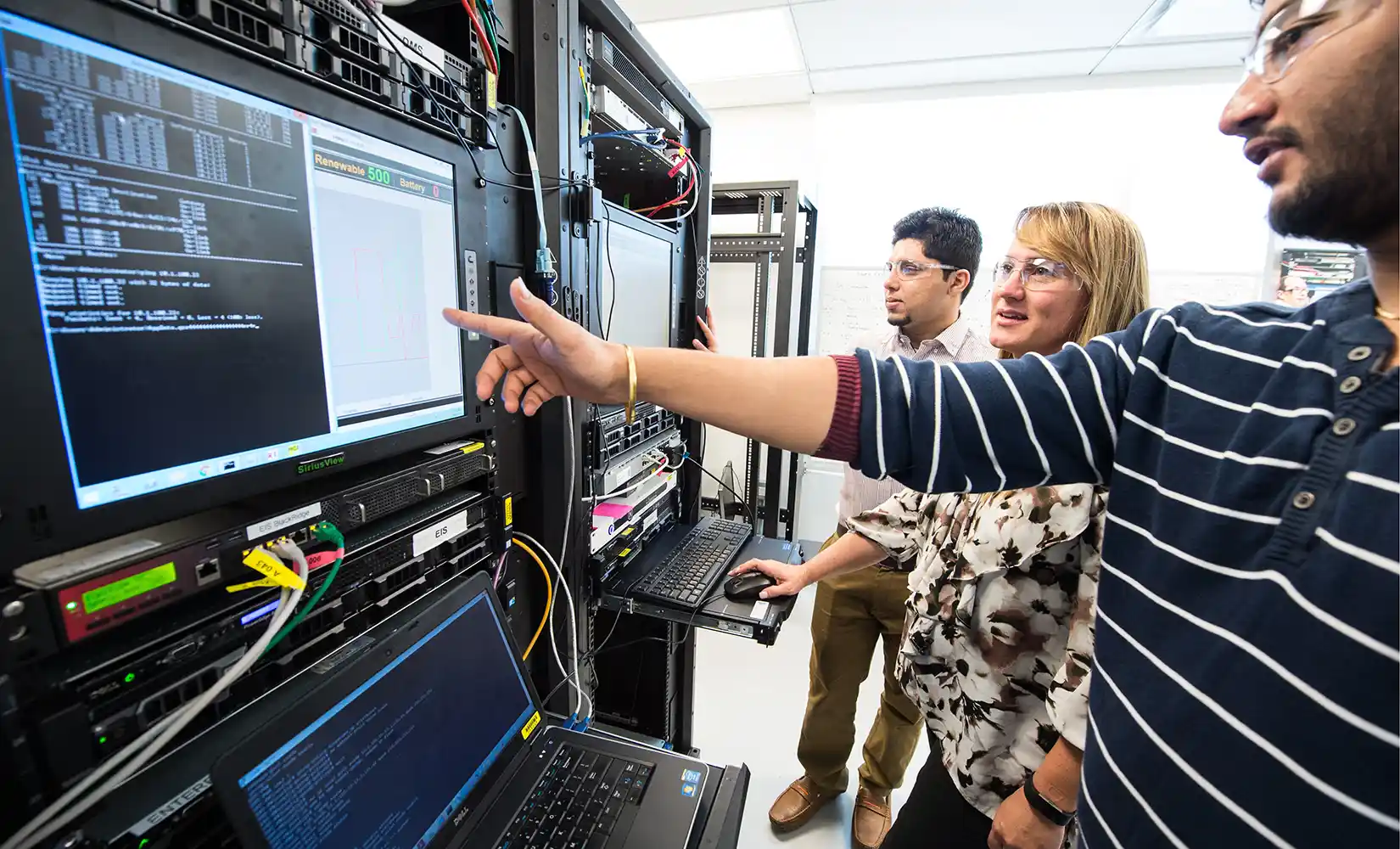 People in goggles look at computers mounted in server towers.