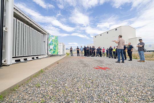 A group of people standing around a stationary battery energy storage system