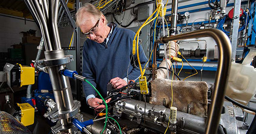 A researcher works on a 4-cylinder spark ignition engine that was converted into a single-cylinder engine for research purposes.