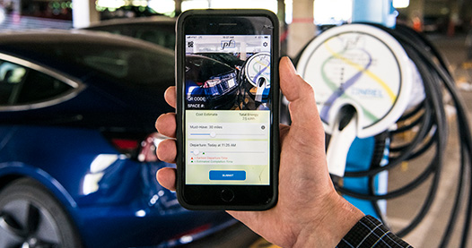 A hand taking a picture with a phone of an electric charging station.