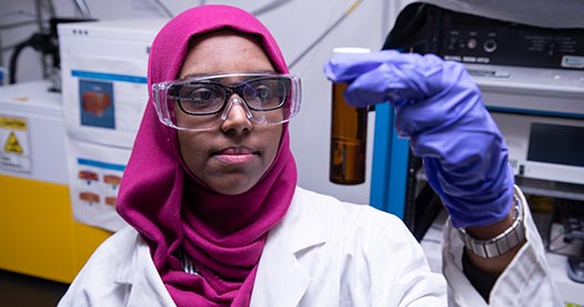 A woman in a lab holding a test tube in the air.