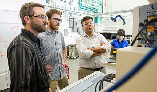 Three researchers examining inverter test waveforms on a computer monitor.