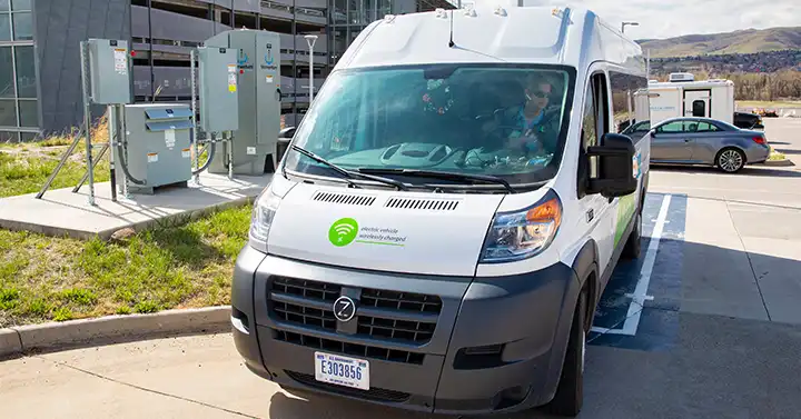 Photo of van parked in a designated spot next to several pieces of boxed equipment near a parking garage