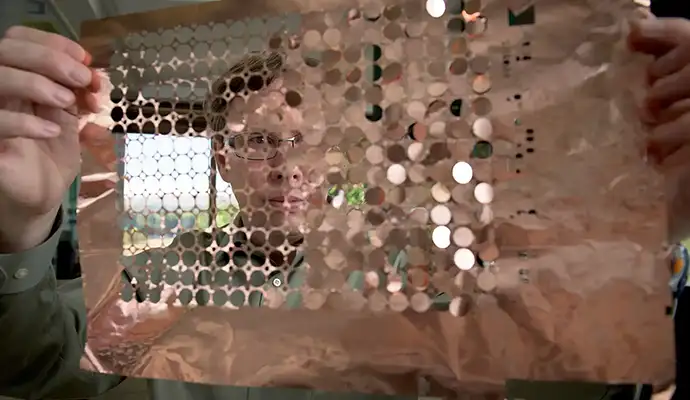 A person holds up a sheet of copper discs.
